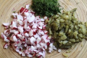 Chopped radishes, chopped pickles and chopped dill on a wooden board. 